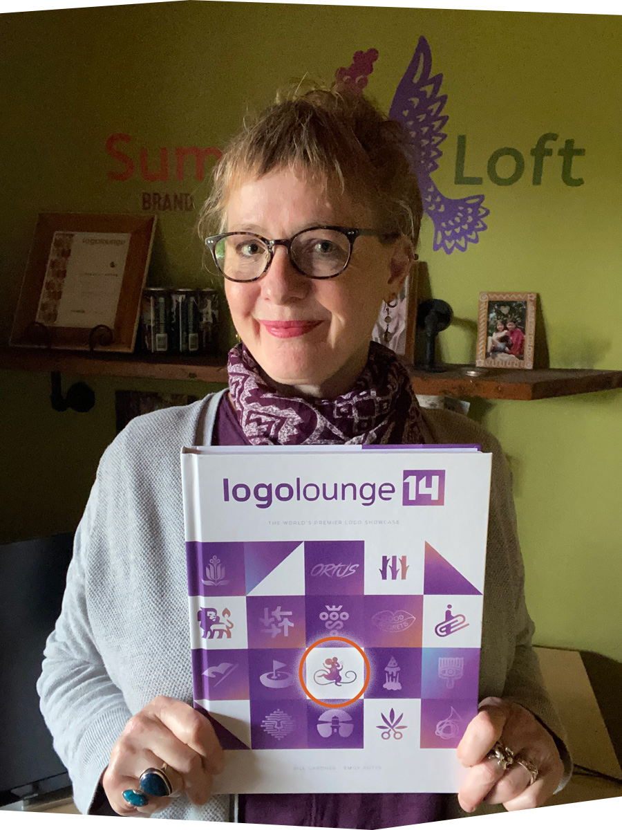 Auni Milne of Sumack Loft holding a copy of LogoLounge 14, featuring her award-winning blue mouse logo on the cover.