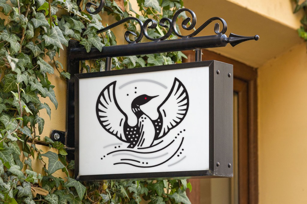 A striking black-and-white loon logo displayed on an elegant outdoor business sign, symbolizing rising and renewal.