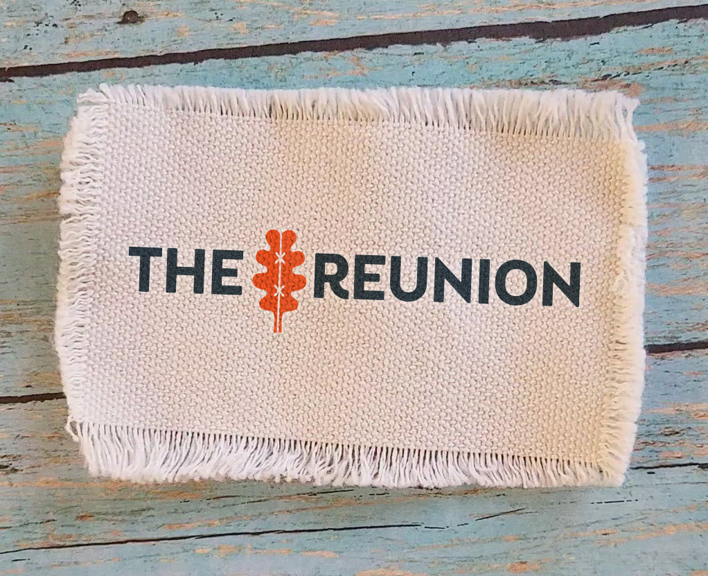 A fabric patch with "The Reunion" logo, featuring an orange oak leaf, embroidered on a textured woven background.