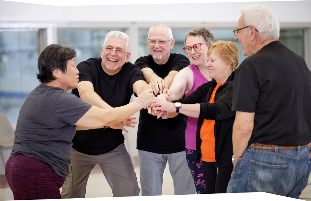 Group of older adults in a team huddle, smiling and celebrating together.