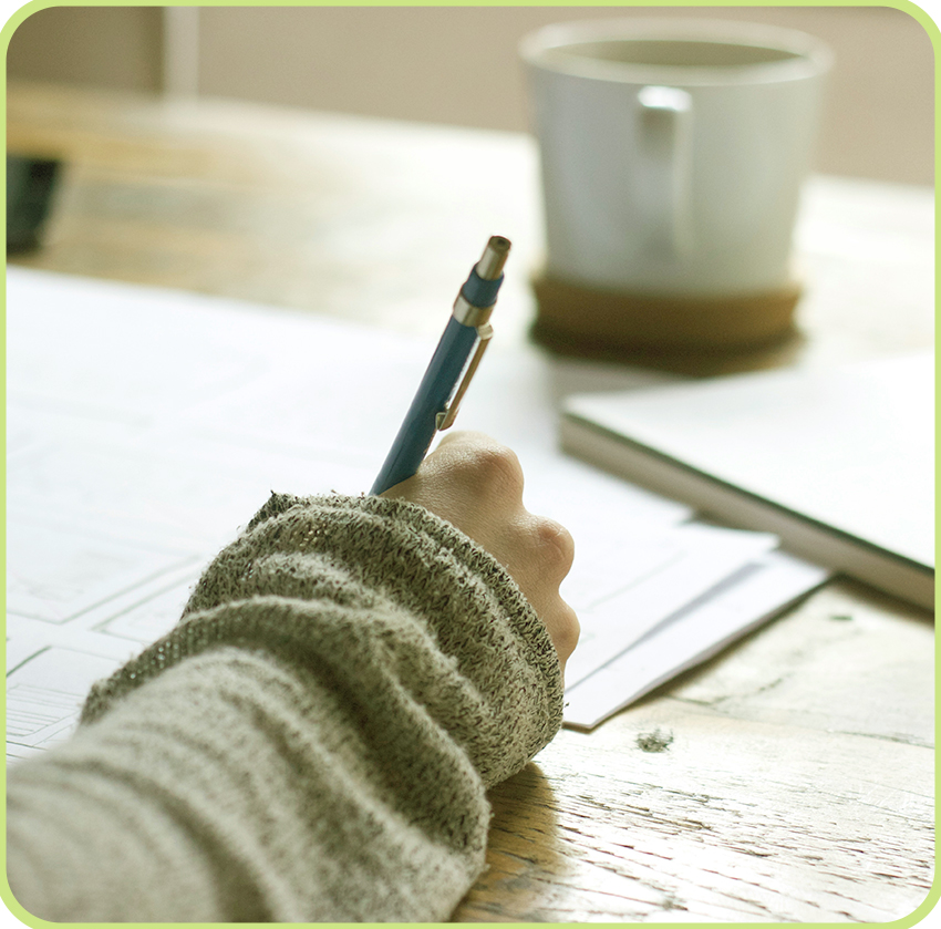 Close-up of someone taking notes during a website planning session, with coffee and sketchpad on wooden desk.